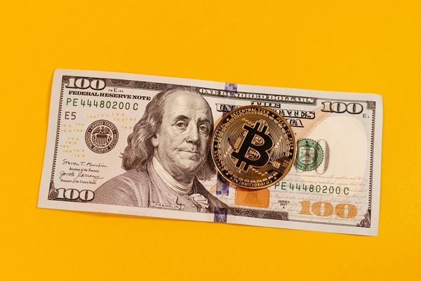 Gold Bitcoin coin on a 100 US dollar bill against a yellow background