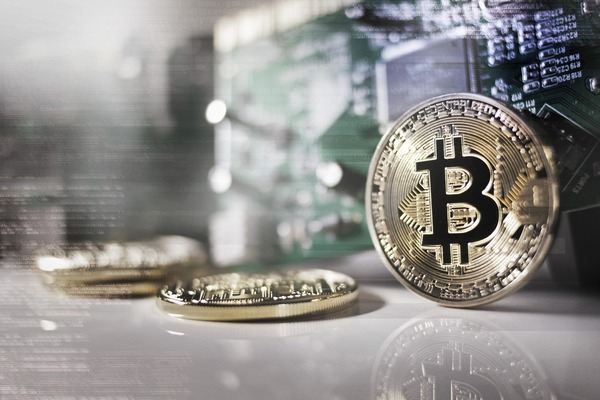 Gold Bitcoin coin standing on a table near a circuit board