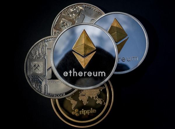 Silver Ethereum coin on top of a stack of crypto coins on black