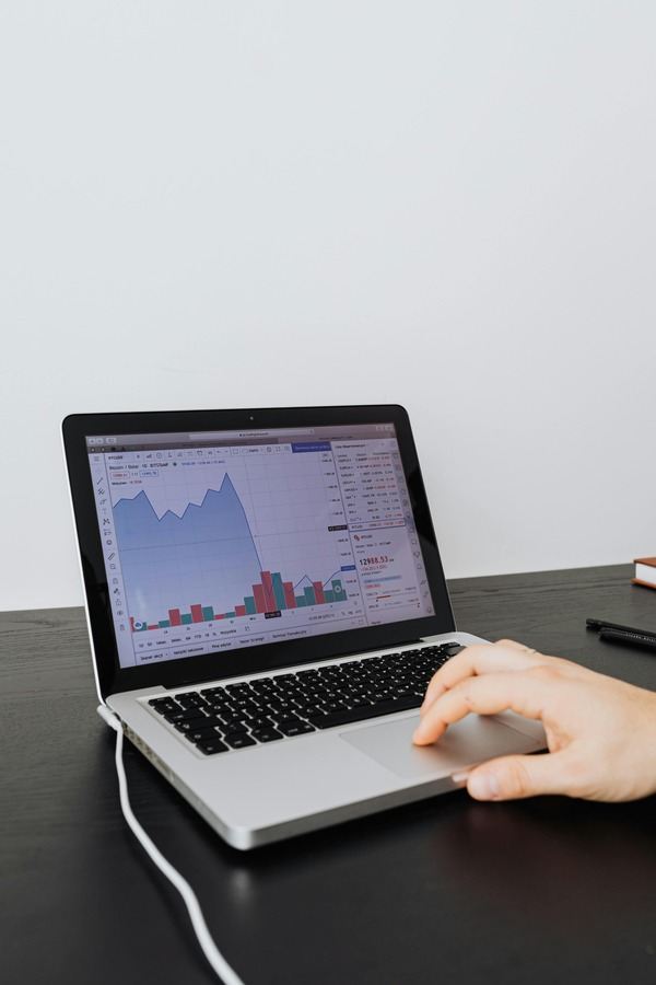 Hand on a laptop showing a financial chart on a dark desk