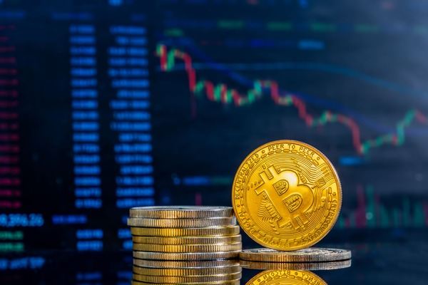 Stack of gold Bitcoin coins in front of a blue market chart
