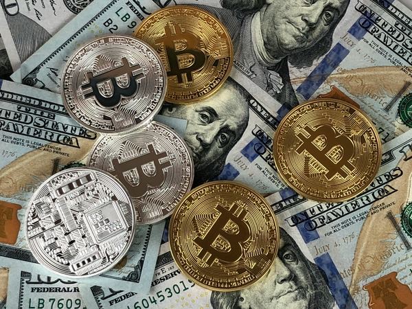 Gold and silver Bitcoin coins scattered over US dollar banknotes