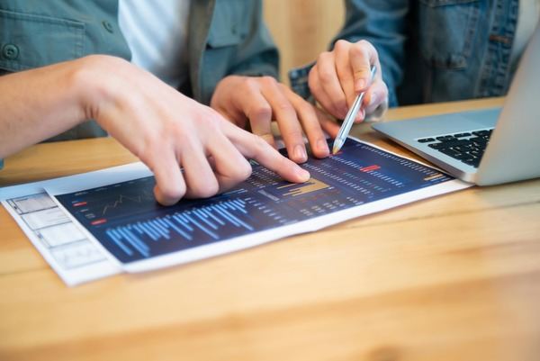 Hands pointing with a stylus at a chart on a tablet beside a laptop