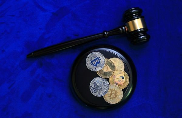 Judge gavel beside a tray of crypto coins on a blue background
