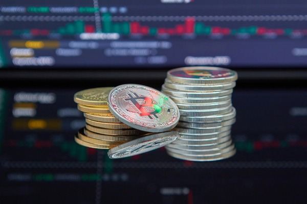 Stacks of silver and gold crypto coins in front of a trading chart
