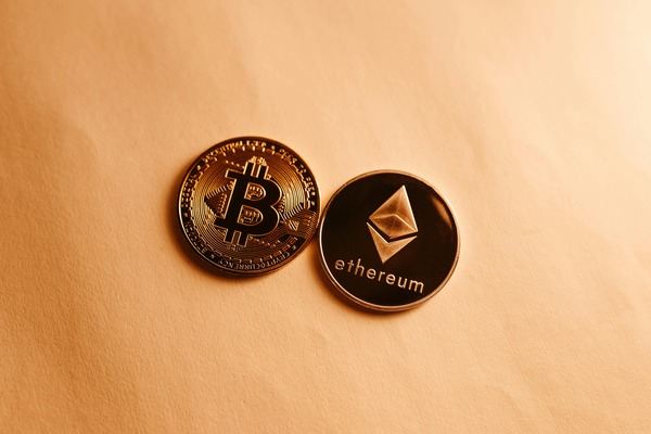 Bitcoin and Ethereum coins lying side by side on a beige surface