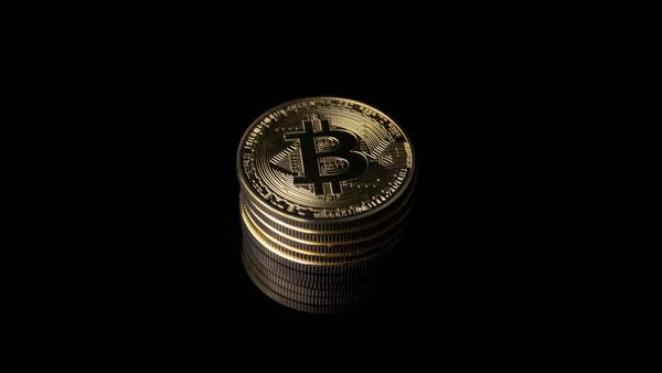 Stack of gold Bitcoin coins reflected on a black surface