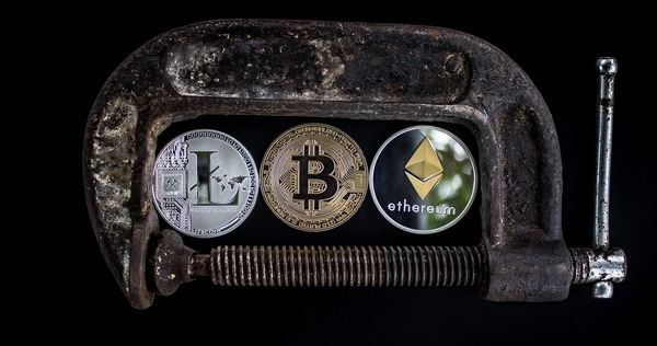 Litecoin, Bitcoin and Ethereum coins held in a rusty metal clamp