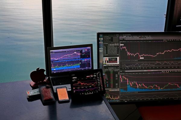 Trading desk with several chart screens in front of a sea view window