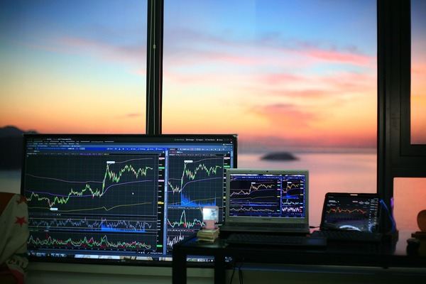 Trading desk with chart monitors in front of a sunset sea view