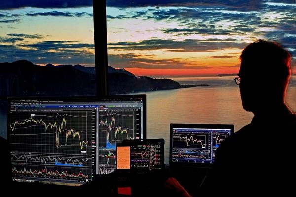 Silhouette of a trader at chart monitors against a sunset sea