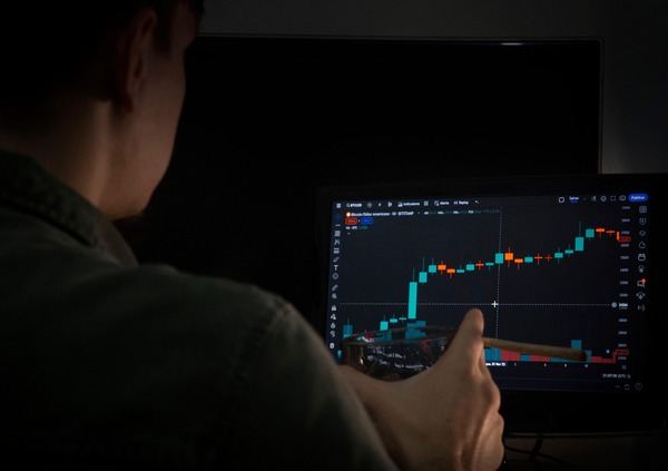Person watching a rising crypto chart on a monitor in a dark room