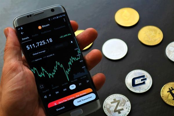 Hand holding a smartphone with a Bitcoin price chart beside crypto coins