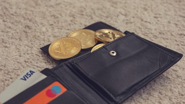 Black leather wallet holding gold Bitcoin coins and bank cards