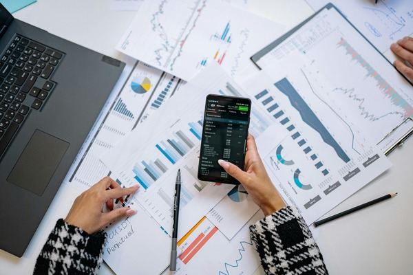 Hands holding a smartphone with a trading app over printed charts