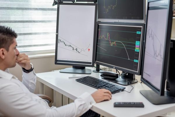 Man reviewing crypto charts across several monitors at a white desk