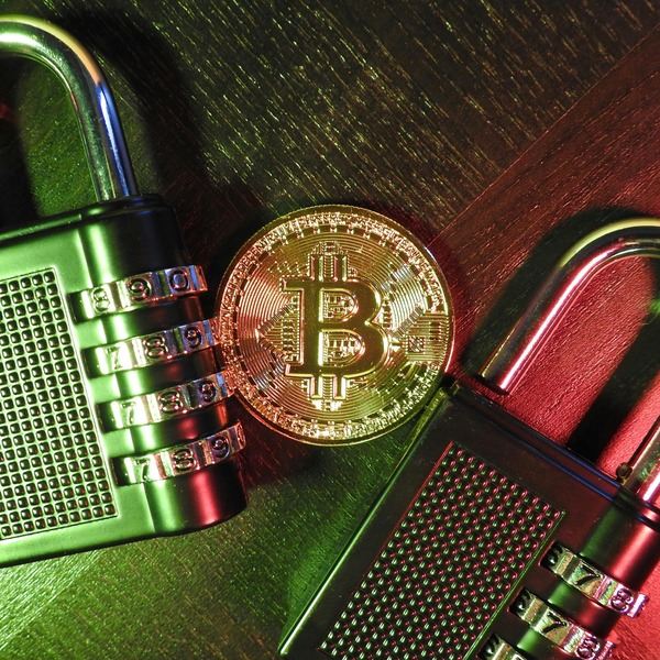Gold Bitcoin coin next to a metal combination padlock