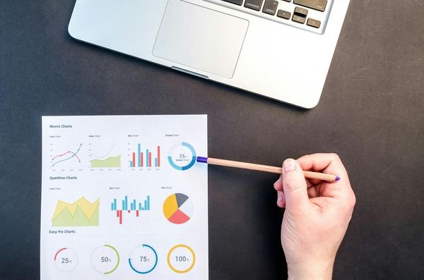 Hand pointing a pencil at printed financial charts next to a laptop