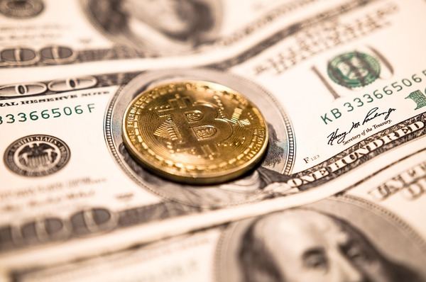 Gold Bitcoin coin lying on US dollar banknotes
