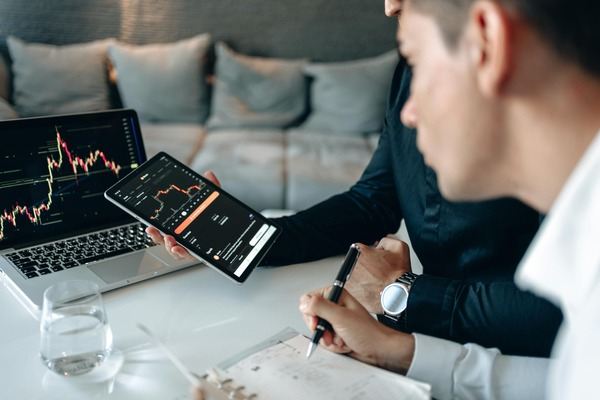 Two traders reviewing crypto charts on a laptop and smartphone